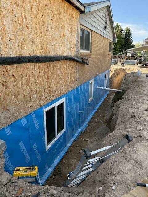 Foundation wall excavated and wrapped, trench open for backfill.