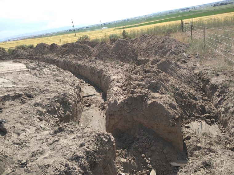 Deep trenches lined with filter fabric with farm fields in the distance