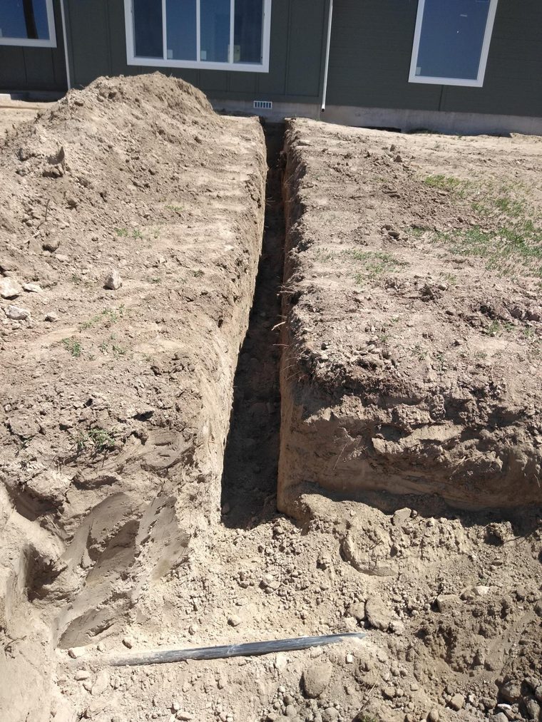 Straight narrow trench dug in dry soil behind a green house