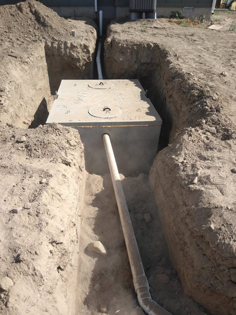 Concrete septic tank set and plumbed, inlet and outlet lines run.