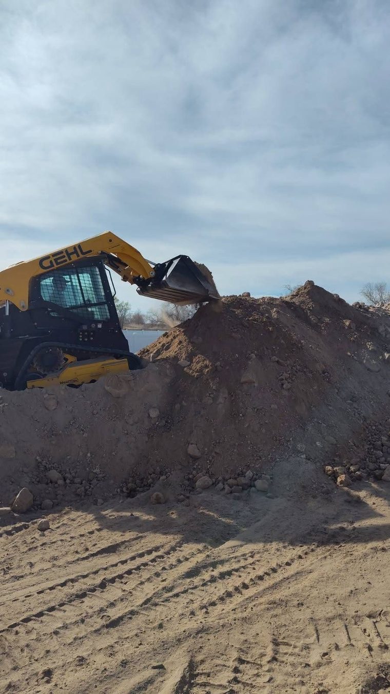Skid steer moving and stockpiling dirt on a site.