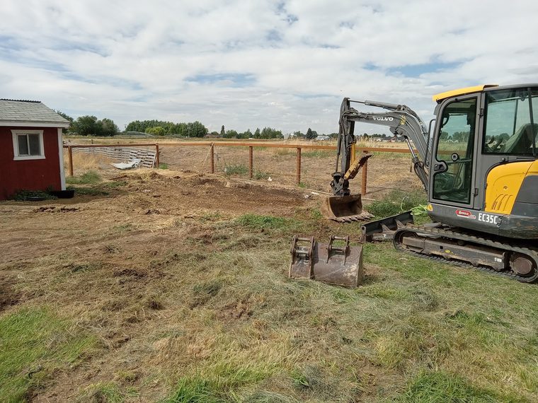 Yellow Volvo mini excavator parked on a graded lot beside a red shed and a spare bucket