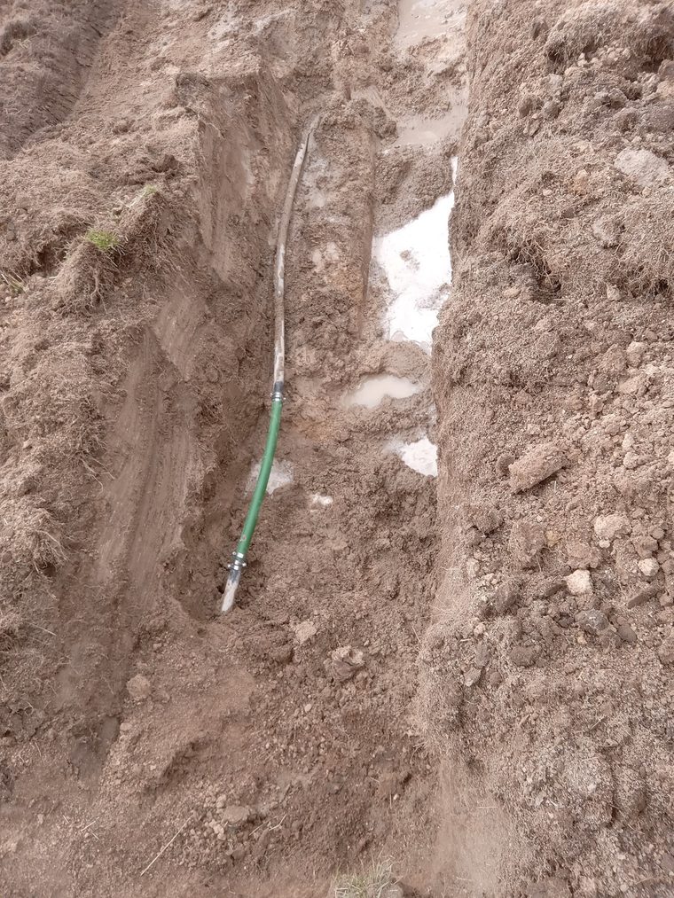 Green poly water line joined to an existing line with couplings inside a dirt trench